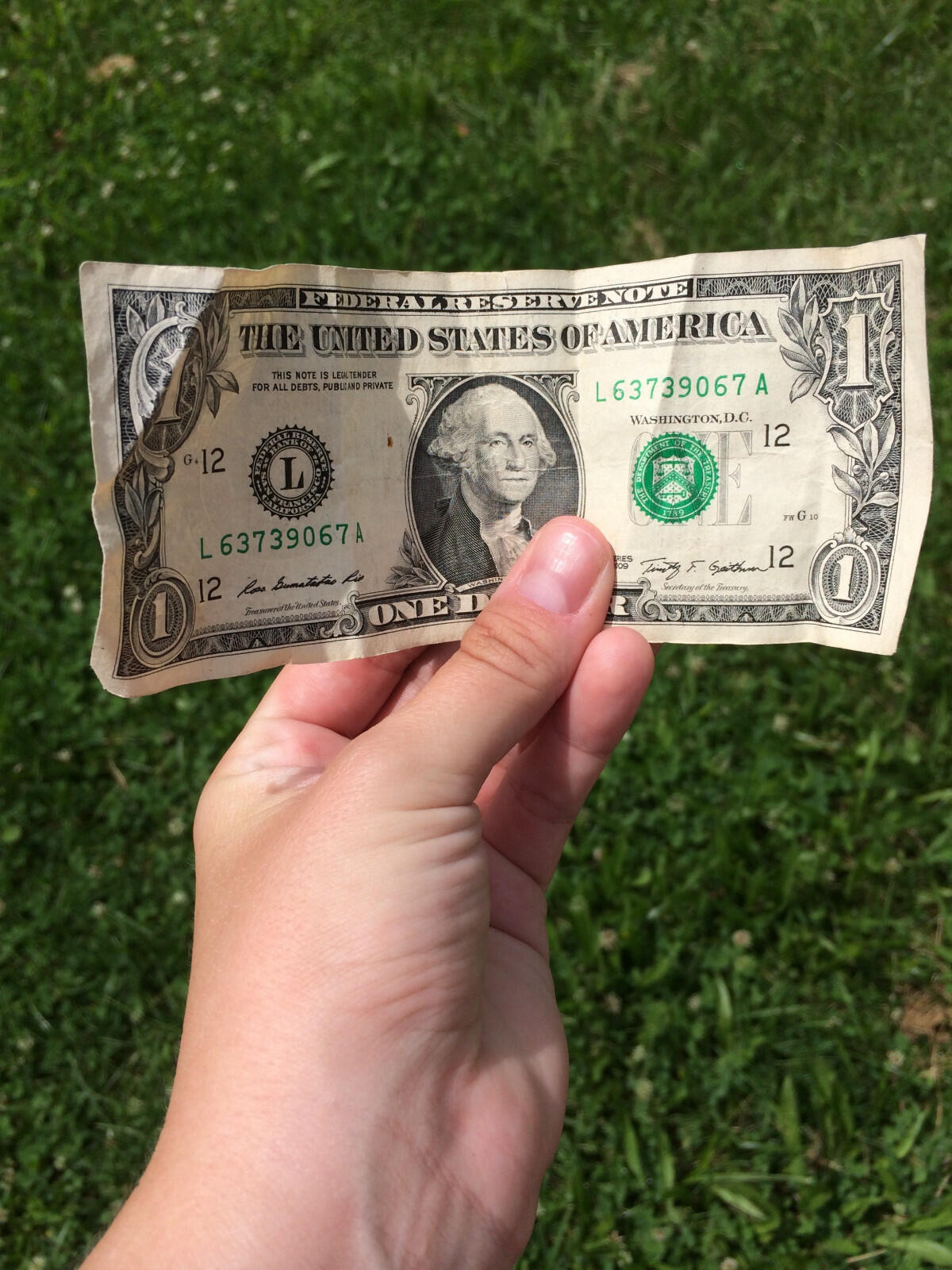 A hand holding a one-dollar bill outdoors