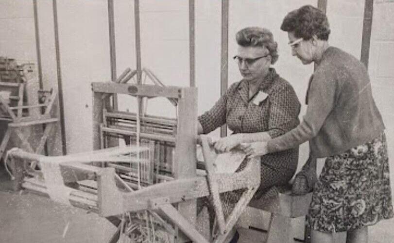 Two women sit at a loom weaving, picture is black and white